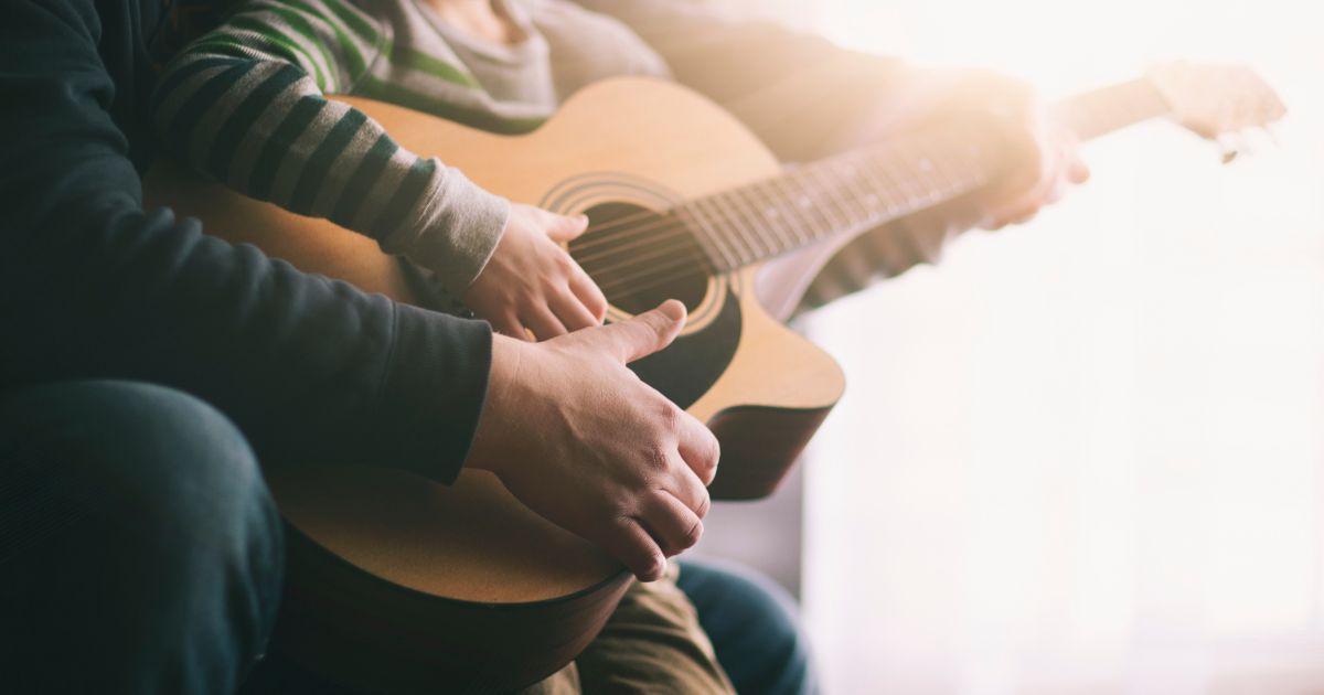 The above stock image is of a father teaching his son to play the guitar.
