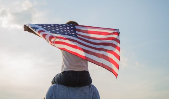 A child sits on a man's shoulder and holds an American flag in the above stock image.