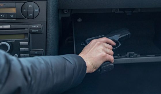 A stock photo shows a man removing a handgun from the glove compartment of his vehicle.
