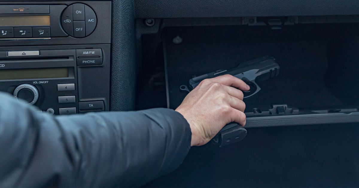 A stock photo shows a man removing a handgun from the glove compartment of his vehicle.