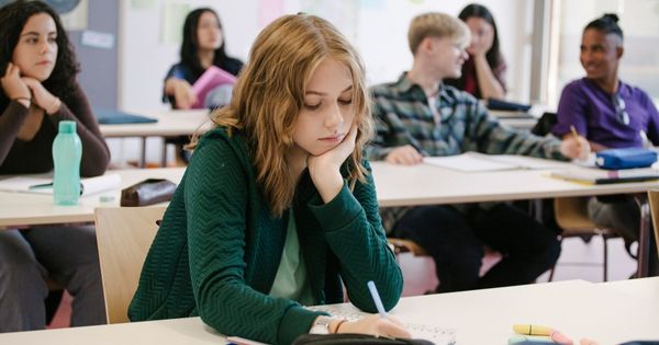 This stock photo shows a student taking notes during class while working in a classroom with her classmates.