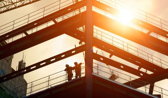 Construction workers are silhouetted by the sun in this stock photo.