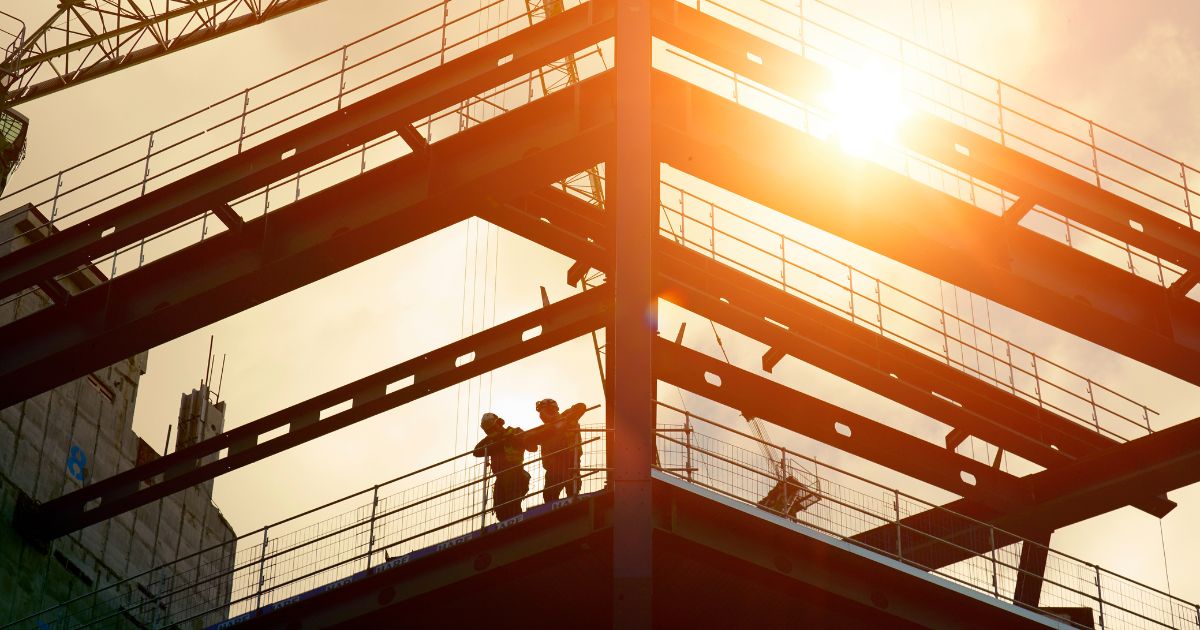 Construction workers are silhouetted by the sun in this stock photo.