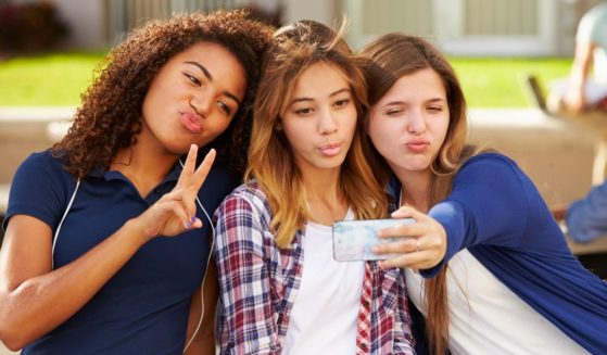 Teenage girls take selfies on a high school campus.