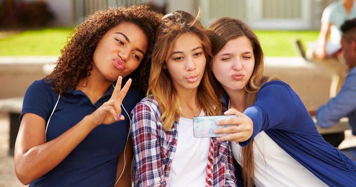 Teenage girls take selfies on a high school campus.