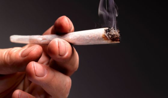 A hand is shown holding a lit marijuana joint.