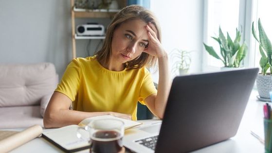 A woman sits in front of a computer, looking a little stressed, in this stock photo.