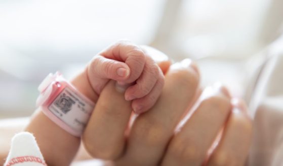 A newborn baby grasps a woman's finger in this stock image.