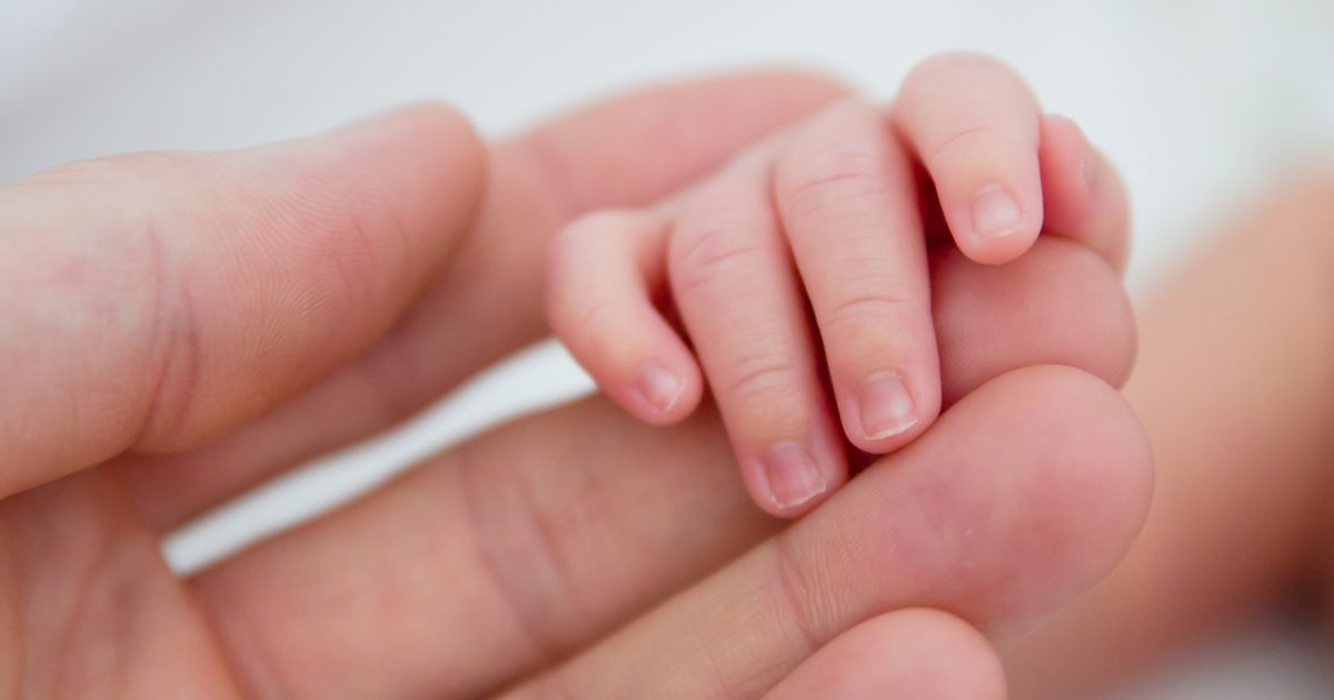 A baby holds a man's finger in this stock image.