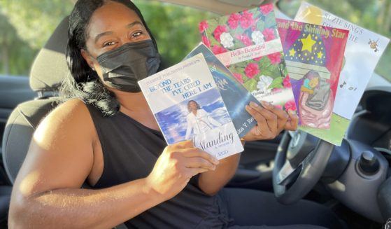 Tomika Reid holds up books that she has authored in her car that she uses to be a Lyft driver in Princeton, New Jersey.
