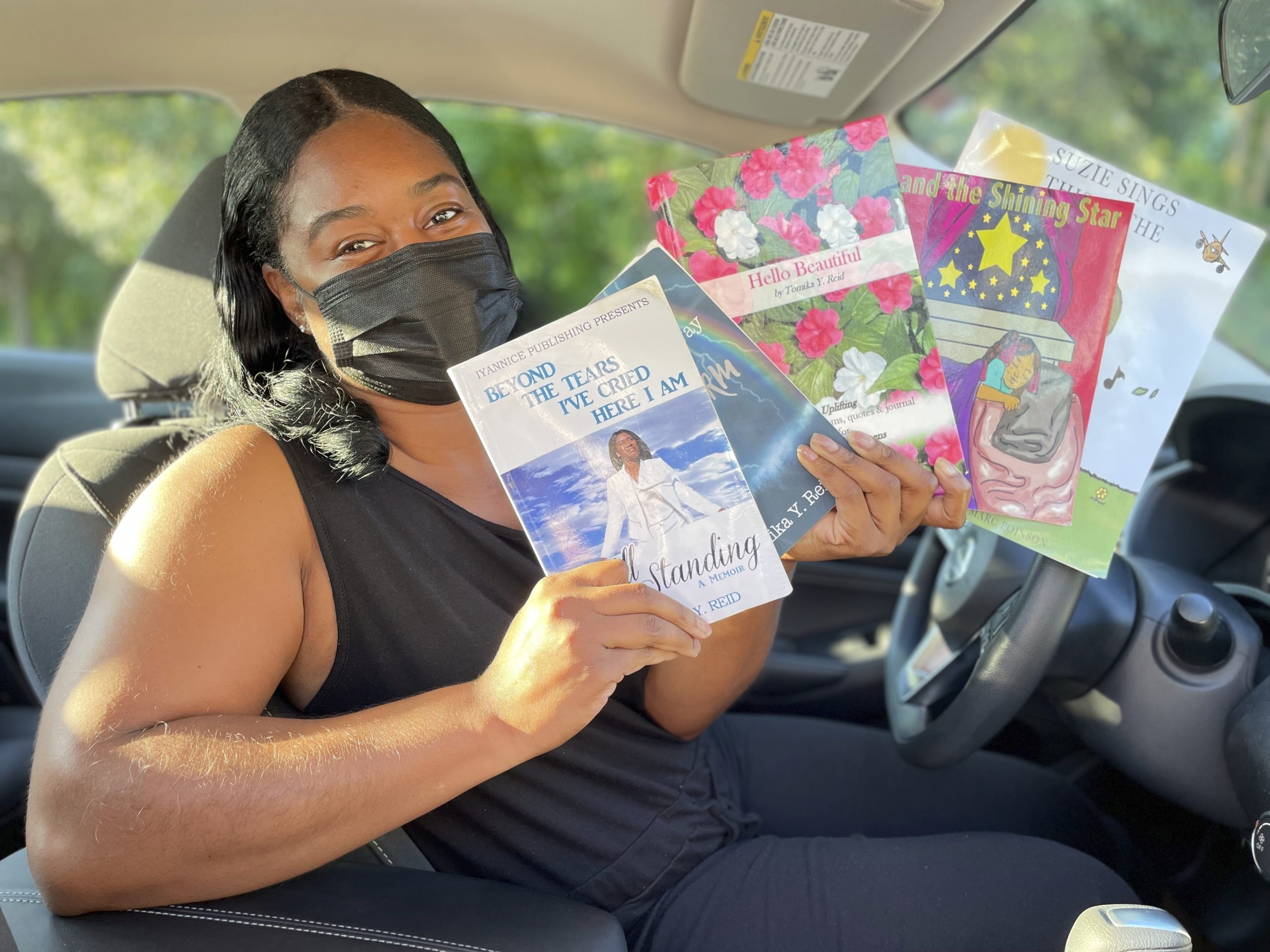 Tomika Reid holds up books that she has authored in her car that she uses to be a Lyft driver in Princeton, New Jersey.