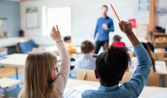 Students raise their hands in a classroom in the above stock image.