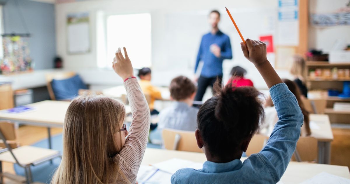 Students raise their hands in a classroom in the above stock image.