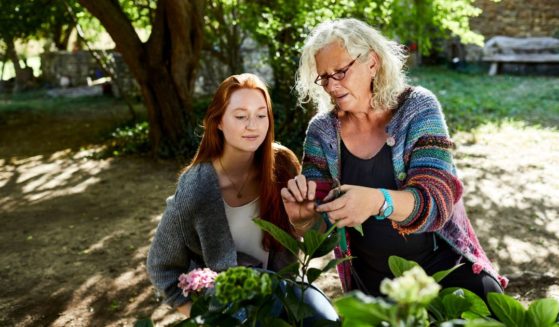 The above stock image is of a senior woman and a young woman examining flowers in a garden.