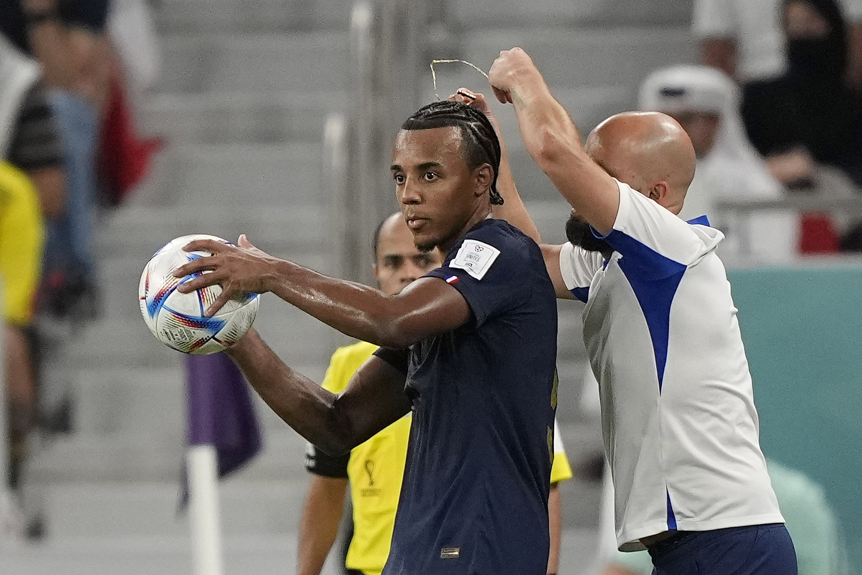 An assistant coach takes off the necklace of France's Jules Kounde during the World Cup soccer match between France and Poland at the Al Thumama Stadium in Doha, Qatar, on Sunday.
