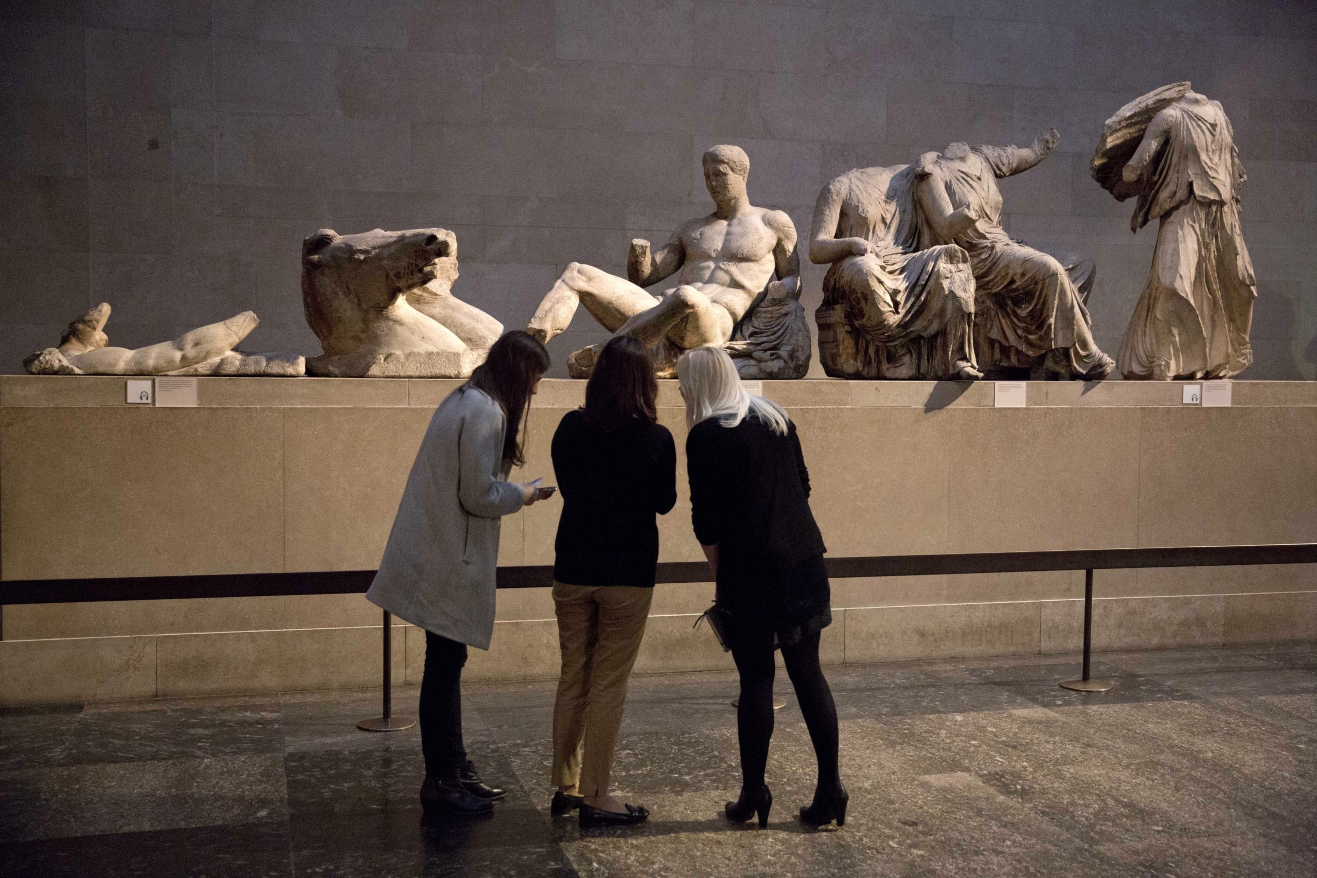 Women stand by a marble statue thought to represent Greek god Dionysos, center, from the east pediment of the Parthenon, during a media photo opportunity to promote an event at the British Museum in London, on Jan. 8, 2015.