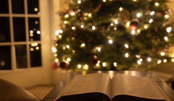 A Bible lays open in front of a Christmas tree in this stock image.