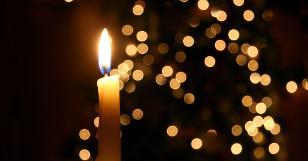 A candle is seen in front of a Christmas tree in this stock image.