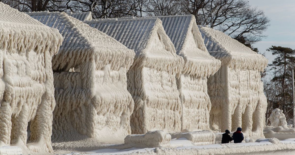 People walk by homes covered in ice at the waterfront community of Crystal Beach in Fort Erie, Ontario, Canada, on Wednesday following a massive snow storm that knocked out power in the area to thousands of residents.