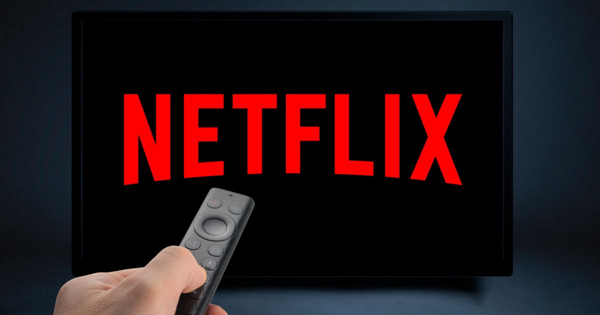 A stock image shows a hand holding a remote control with the Netflix logo on a TV screen.