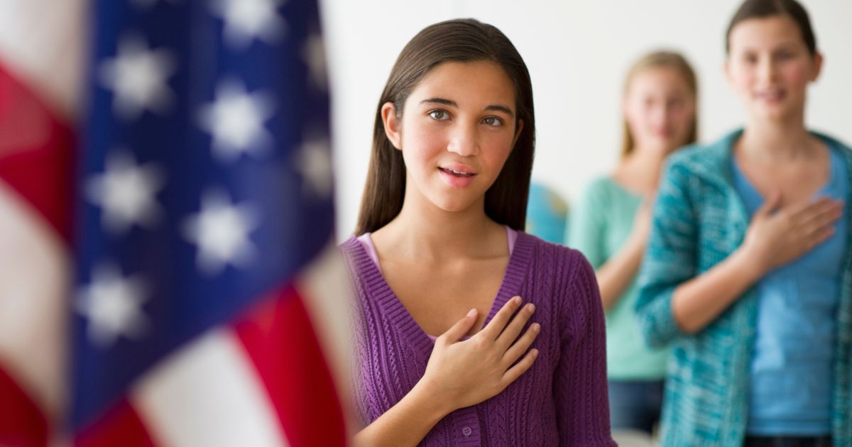 A girl recites the Pledge of Allegiance in the above stock image.