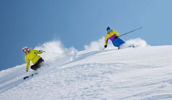 Two skiers ski down a snowy slope