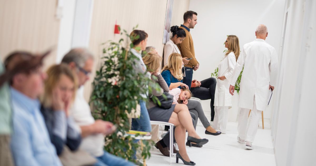 A stock photo shows a medical clinic waiting room full of patients.