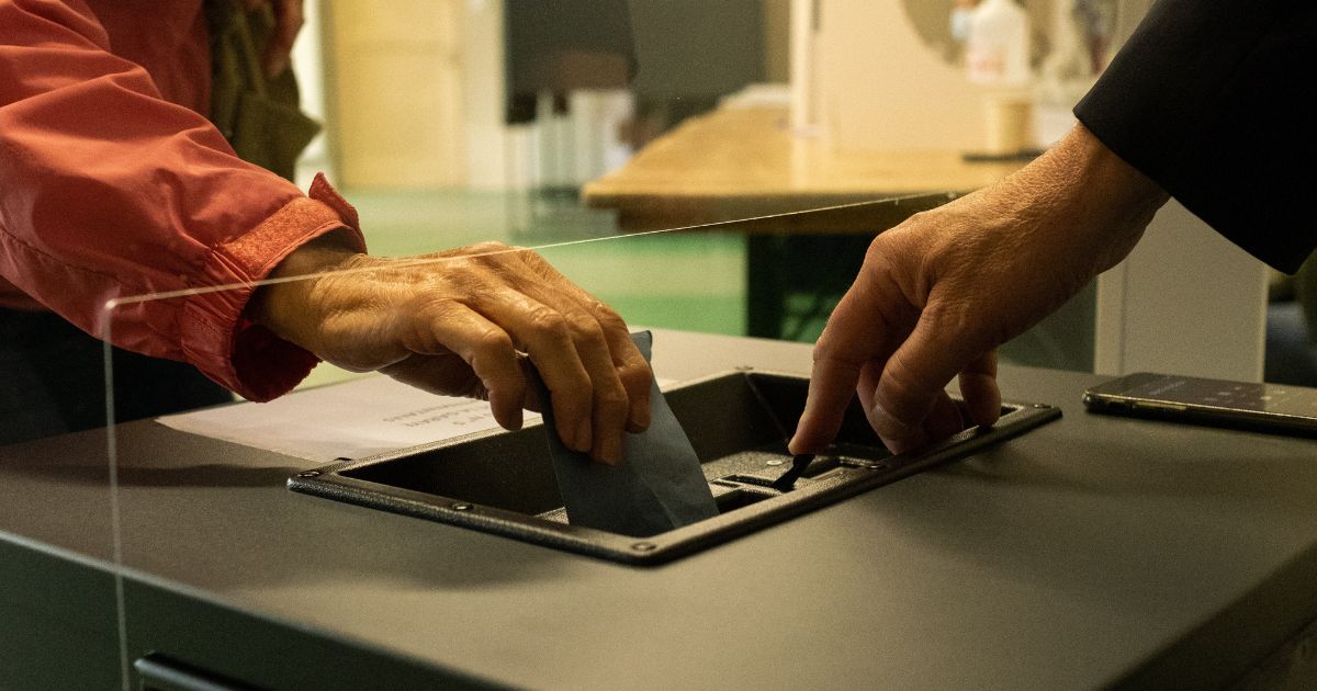 This conceptualized image shows an older woman putting a ballot into a box to be counted.