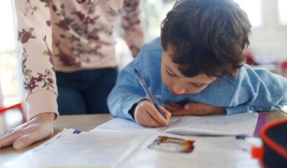 A mother watches her son do schoolwork in the above stock image.