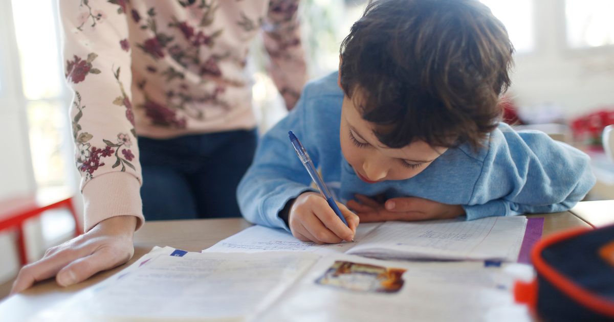 A mother watches her son do schoolwork in the above stock image.