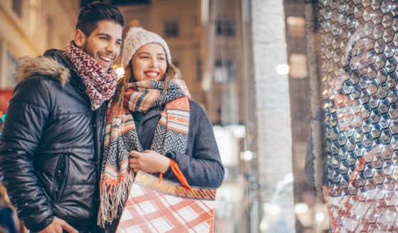 This stock photo shows a young couple going Christmas shopping together, standing in front of a store window.