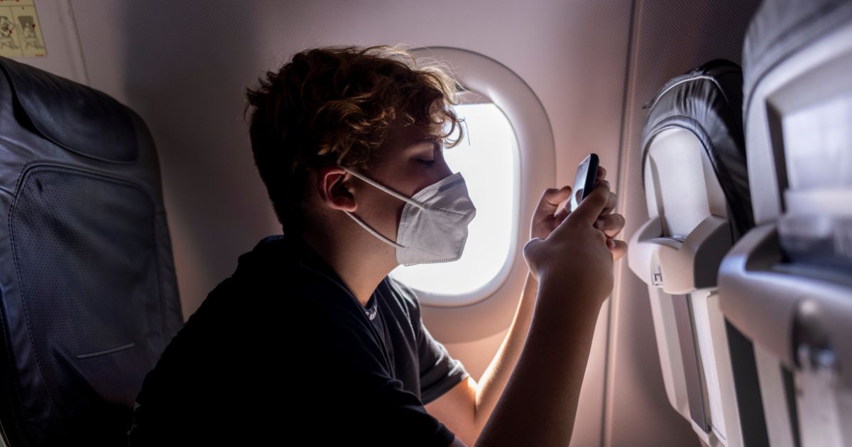 A teenage boy is using a smartphone on an airplane in this stock image.