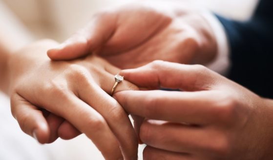 A groom puts a wedding ring on his bride in this stock image.