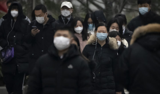 Commuters wearing masks walk along a street in the central business district in Beijing Thursday.