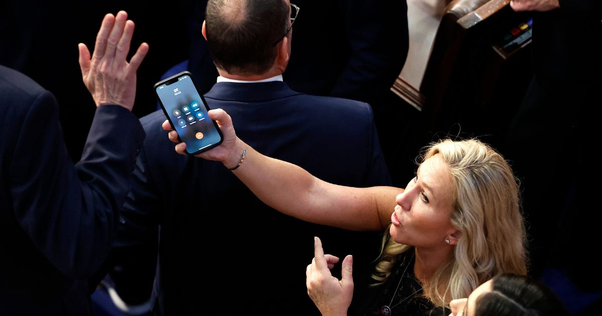 U.S. Rep.-elect Marjorie Taylor Greene (R-GA) offers a phone with the initials "DT" to Rep.-elect Matt Rosendale (R-MT) in the House Chamber during the fourth day of voting for Speaker of the House at the U.S. Capitol Building on January 6, 2023 in Washington, DC.