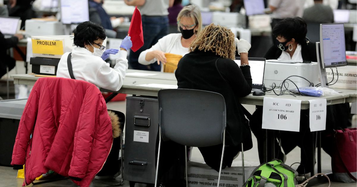 Election workers sort absentee ballots in Detroit during the 2022 general election in November. A new whistleblower complaint alleges that a Michigan election software firm stored poll workers’ private data, including their Social Security numbers, in China.