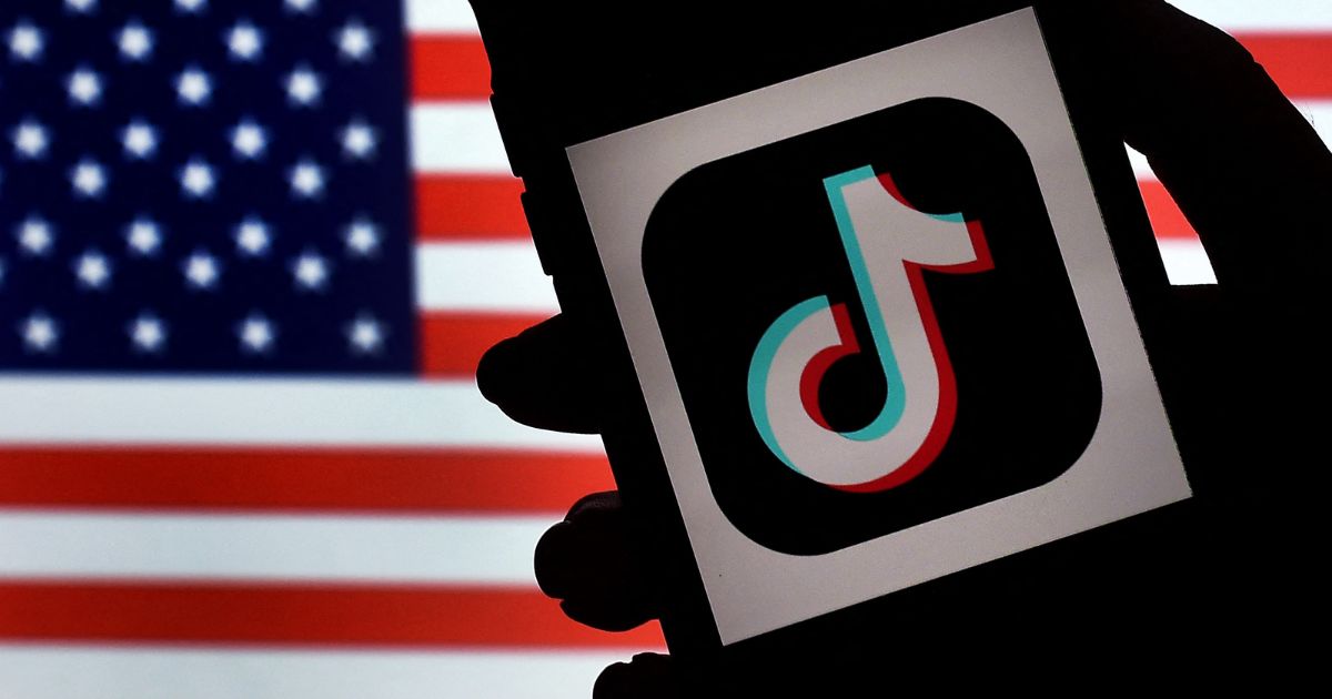 In this photo illustration, the social media application logo, TikTok is displayed on the screen of an iPhone with an American flag background.