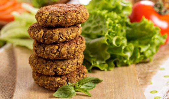 A stock photo shows vegan patties with lentils and pistachios stacked on a cutting board.