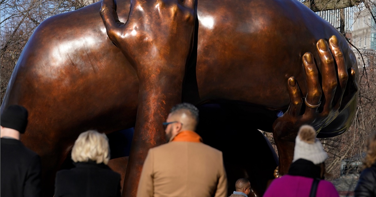Viewers stand near the 20-foot-high bronze sculpture "The Embrace," a memorial to Dr. Martin Luther King Jr. and Coretta Scott King, in the Boston Common on Tuesday in Boston.