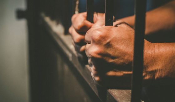 A man grasps the bars of a prison cell in this stock image.