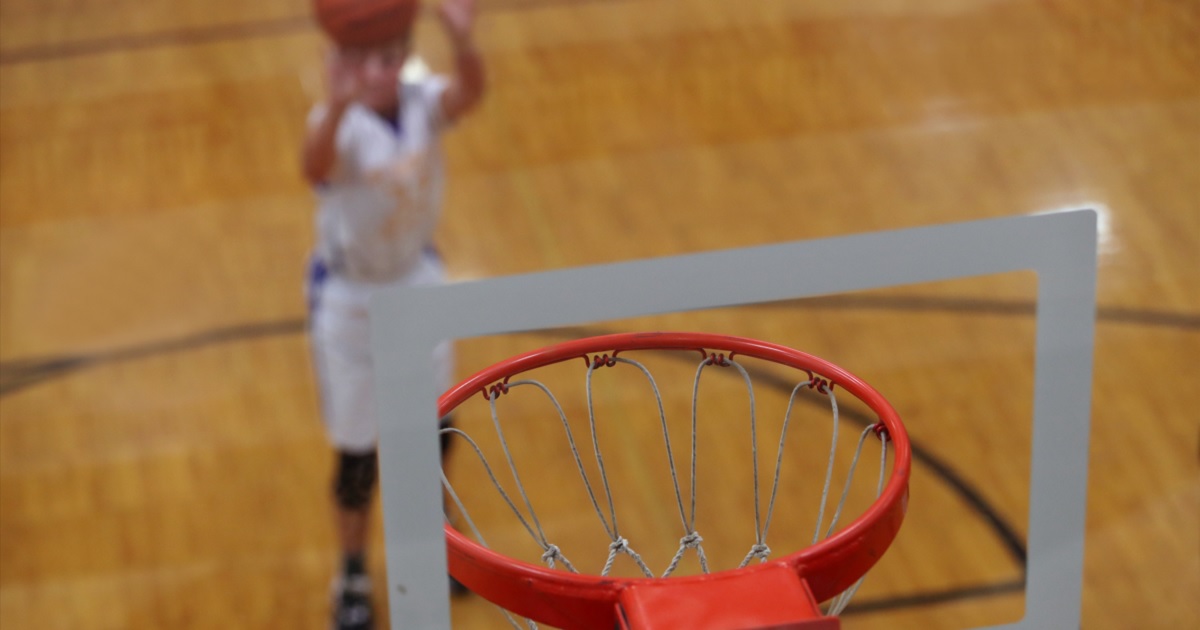 A basketball player making a shot is viewed from above the rim.