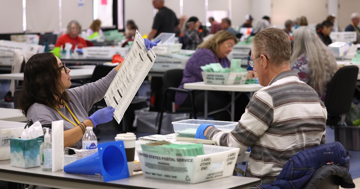 An elections worker inspects a mail-in ballot prior to tabulation at the Maricopa County Tabulation and Election Center on Nov. 6, 2022, in Phoenix.