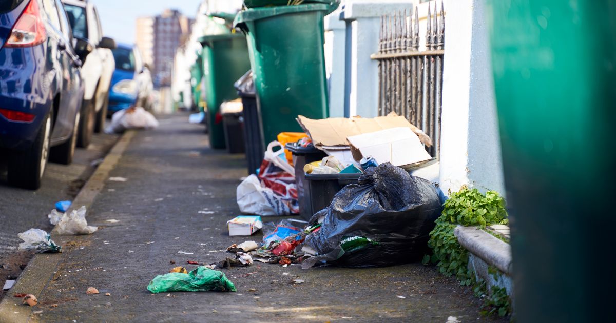 This stock photo depicts trash overflowing from trash cans and covering the sidewalks in a city, a problem that is taking over many major American cities.