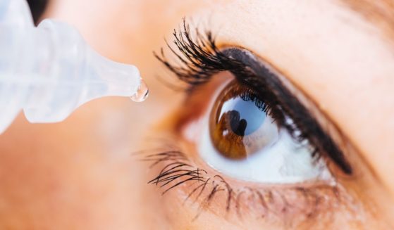 A stock photo shows a woman putting eye drops in her eye.