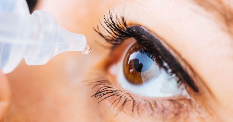 A stock photo shows a woman putting eye drops in her eye.
