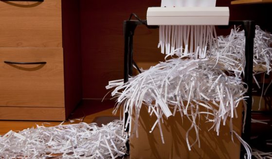 This stock photo depicts documents being shredded into a box in an office.