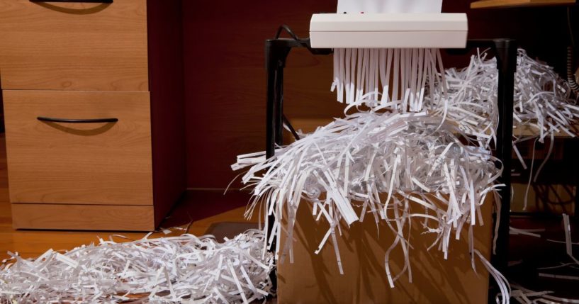 This stock photo depicts documents being shredded into a box in an office.