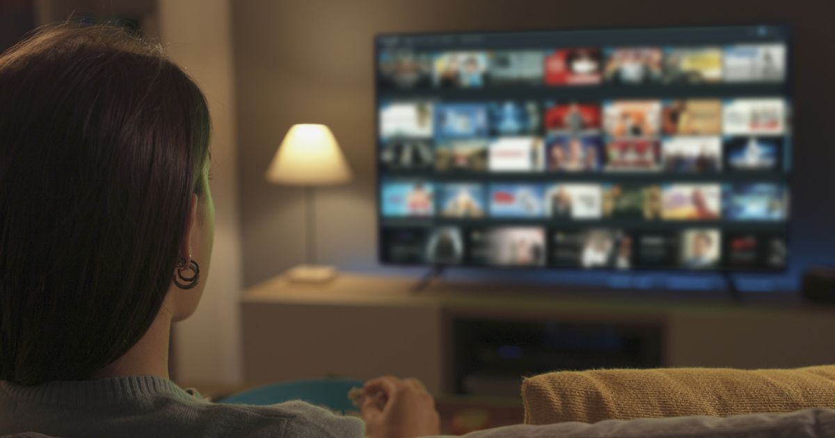 A stock photo shows a woman looking at video options on her TV screen.