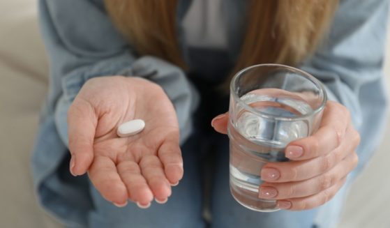 A woman holds a pill and a glass of water in this stock image.