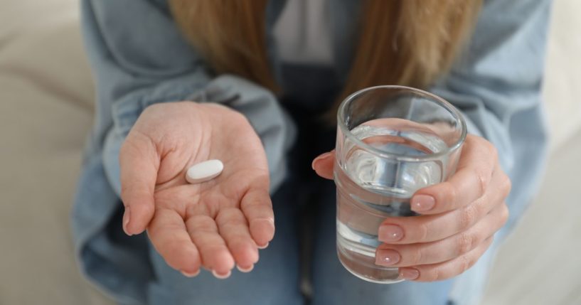 A woman holds a pill and a glass of water in this stock image.
